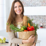Beautiful young woman with vegetables in grocery bag at home.